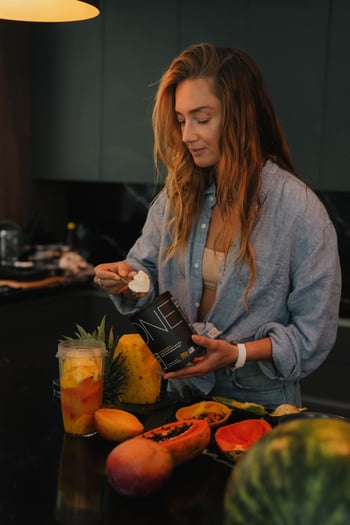 Surf and lifestyle creator preparing a Just Protein smoothie in a tropical-fruit kitchen setup - ingredient-honest product launch content