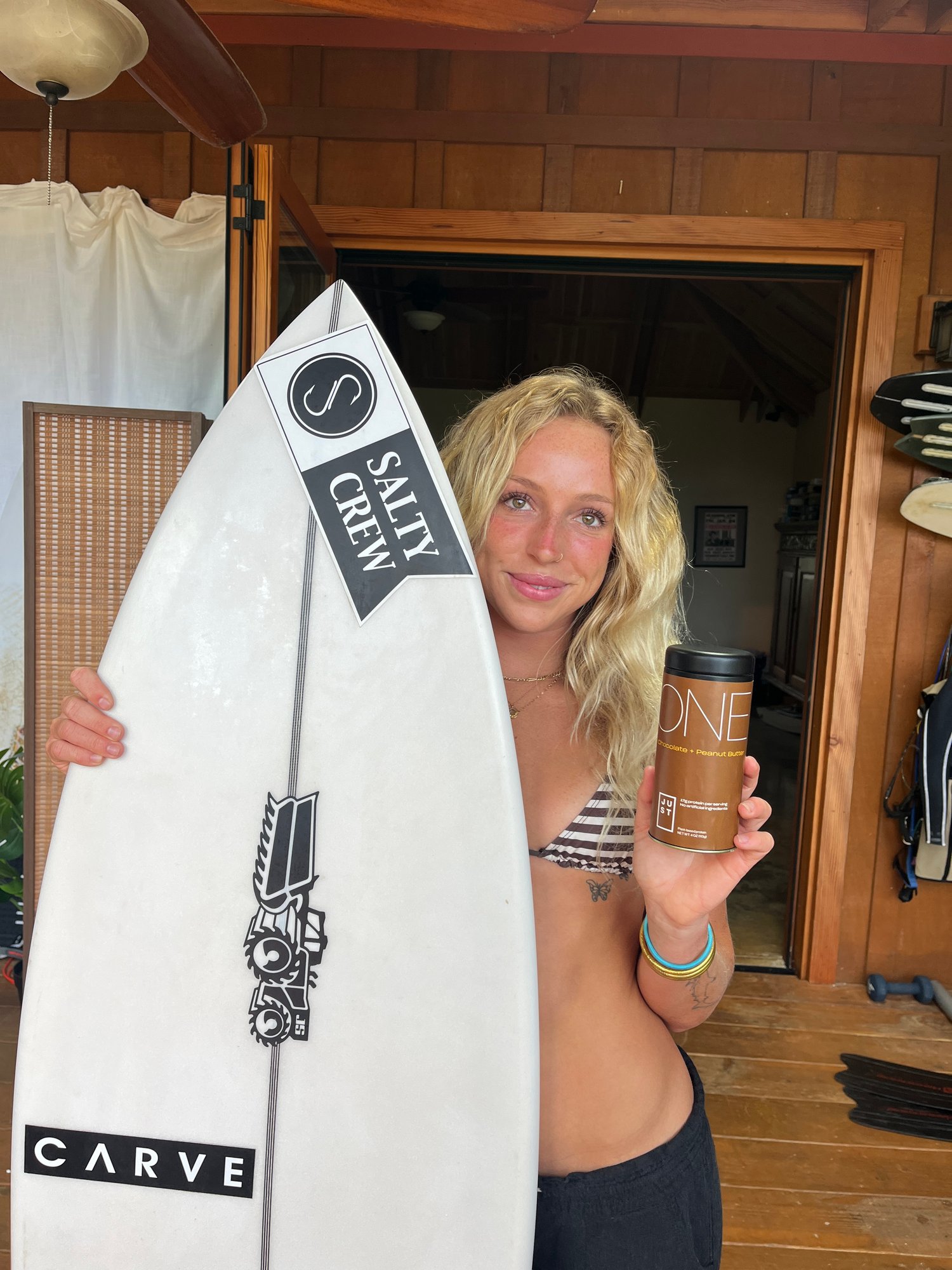 Pro surfer Ellie Brown holding Just Protein next to her Salty Crew surfboard for the Just Protein product launch campaign